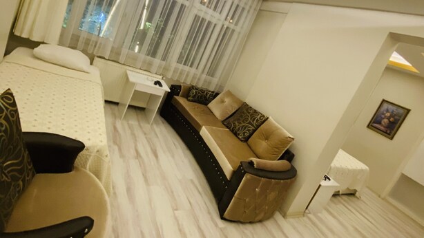 A modern hotel room with a curved sofa, a small white table, and a bed with a white headboard. - Royal Otel (Tokat)