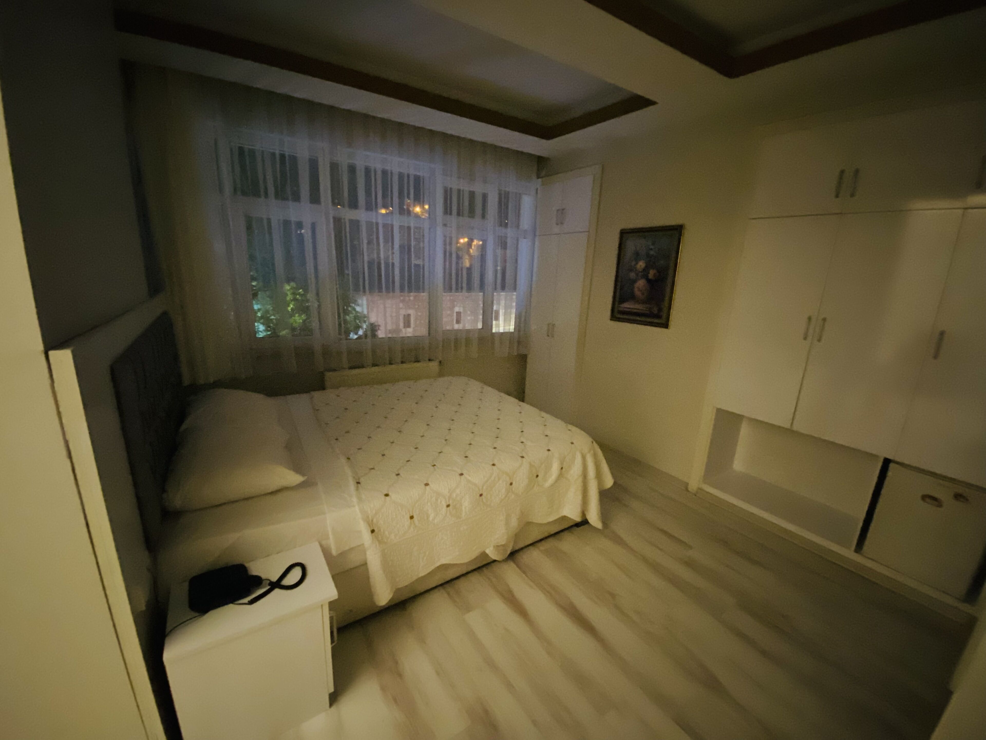 A bedroom with a bed, a nightstand, a wardrobe, and a window with curtains.