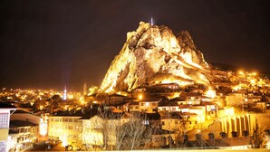A mountain with a tower on top, surrounded by illuminated buildings. - Royal Otel (Tokat)