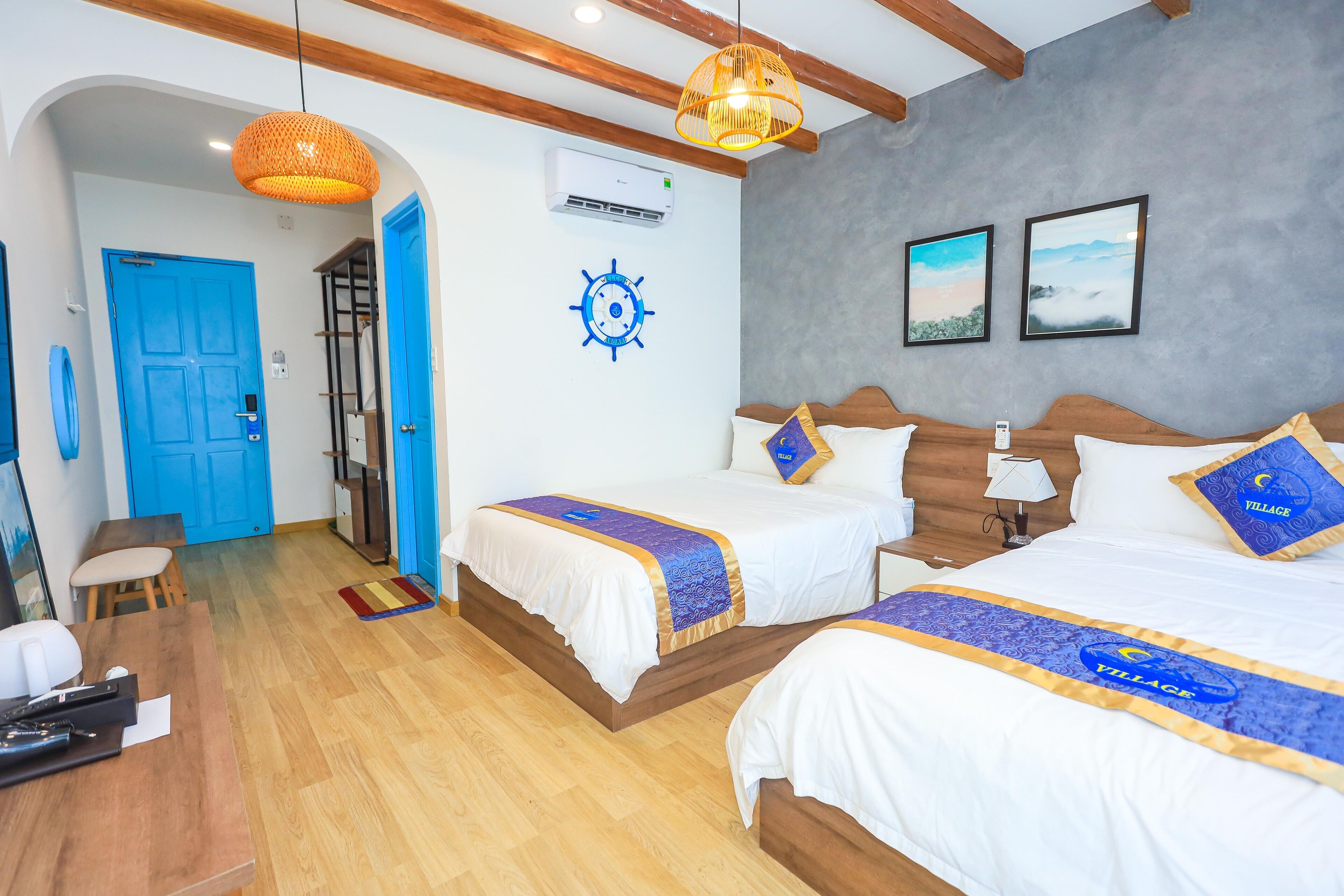Habitación de hotel con dos camas, cabeceros de madera, una puerta azul, aire acondicionado de pared y un ventilador de techo.