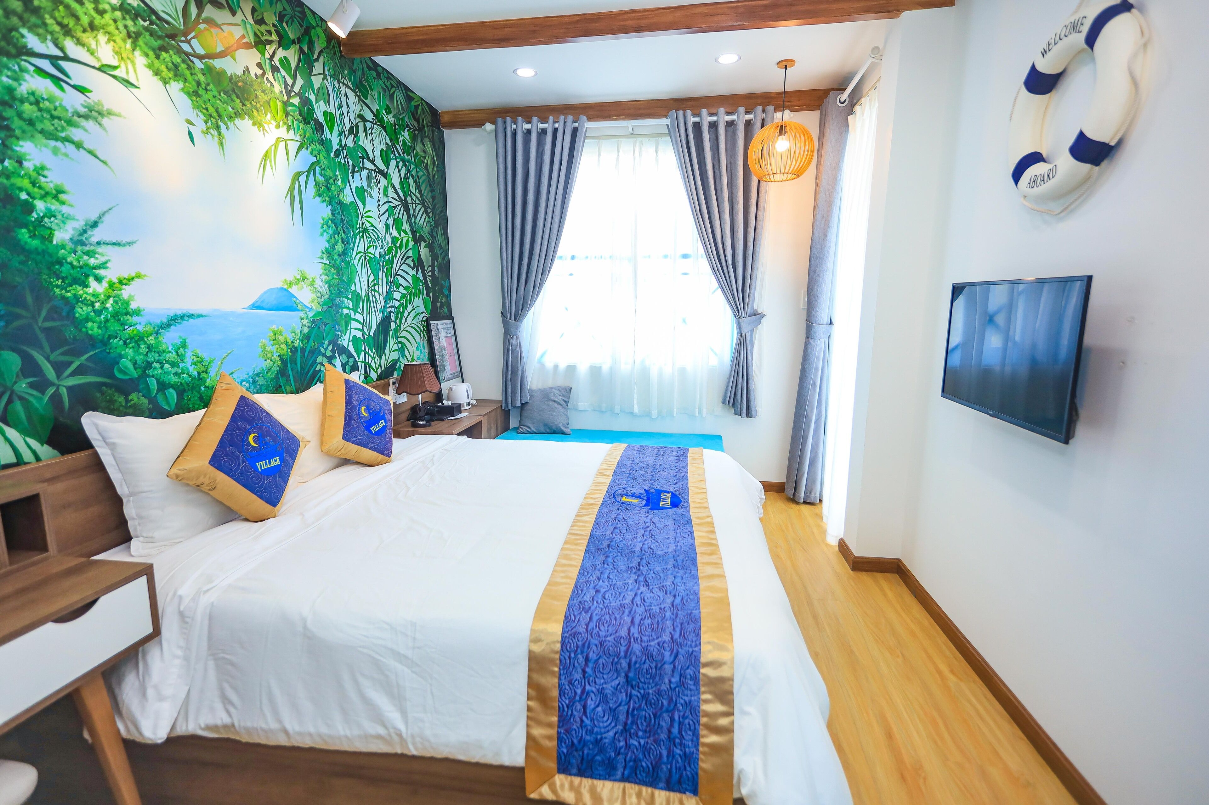 A hotel room with a bed, a nightstand, a wall-mounted TV, a life preserver, and a view of the sea through the window.