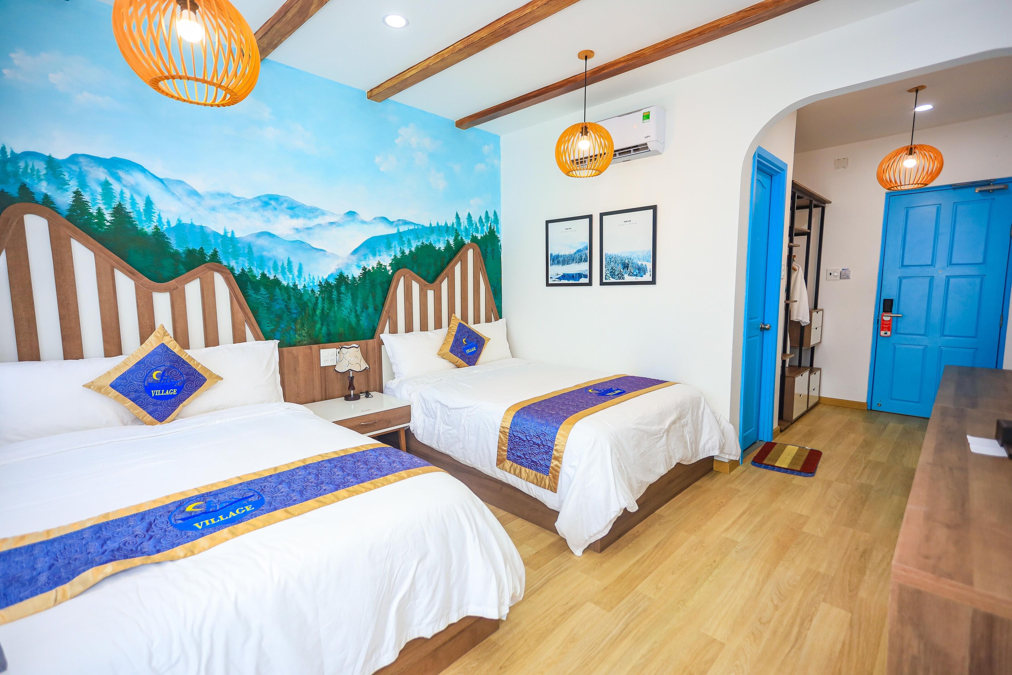 Een hotelkamer met twee bedden, een muurschildering van bergen, houten balken en een blauwe deur.