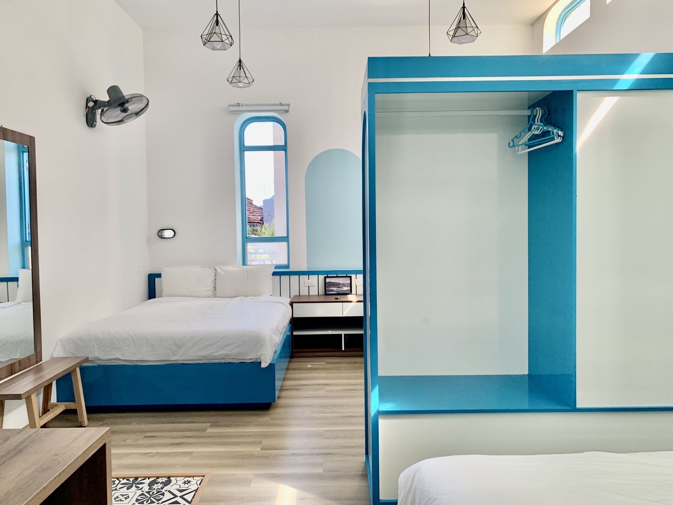 A modern bedroom with a large bed, a smaller bed, a desk, and a wardrobe.