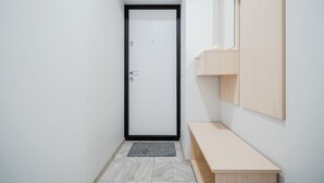 Un pasillo estrecho con una puerta blanca, un pequeño banco y un armario de madera adosado a la pared.
