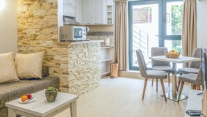 Un appartement moderne doté d’un mur d’accent en pierre, d’une kitchenette, d’un coin repas avec une table et des chaises, et d’un canapé avec des coussins.