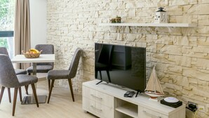Un salon moderne avec un mur en pierre, un téléviseur à écran plat, une table à manger avec des chaises et une petite étagère ornée d’objets décoratifs.