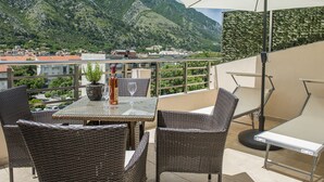 A terrace with wicker furniture, a table, and an umbrella. - Stylish Apartment With Balcony & Pool Access Near The Historical Town (Kotor)