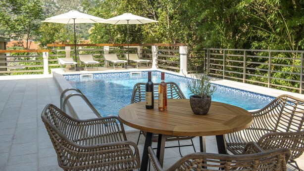 A poolside area with a table, chairs, and two umbrellas. - Stylish Apartment With Balcony & Pool Access Near The Historical Town (Kotor)