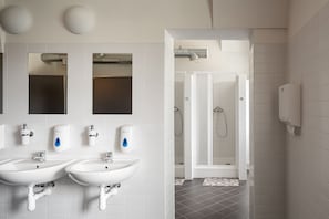 Bathroom features two sinks with faucets and soap dispensers, a shower area with a glass door, and a tiled floor.