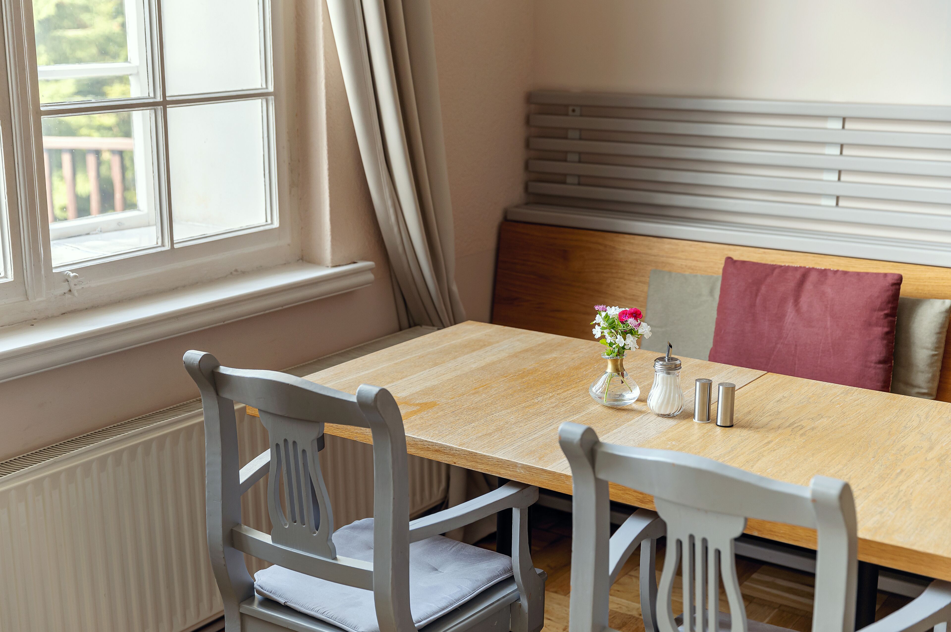 A dining area with a wooden table, four chairs, a vase with flowers, salt and pepper shakers, and a bench with cushions.