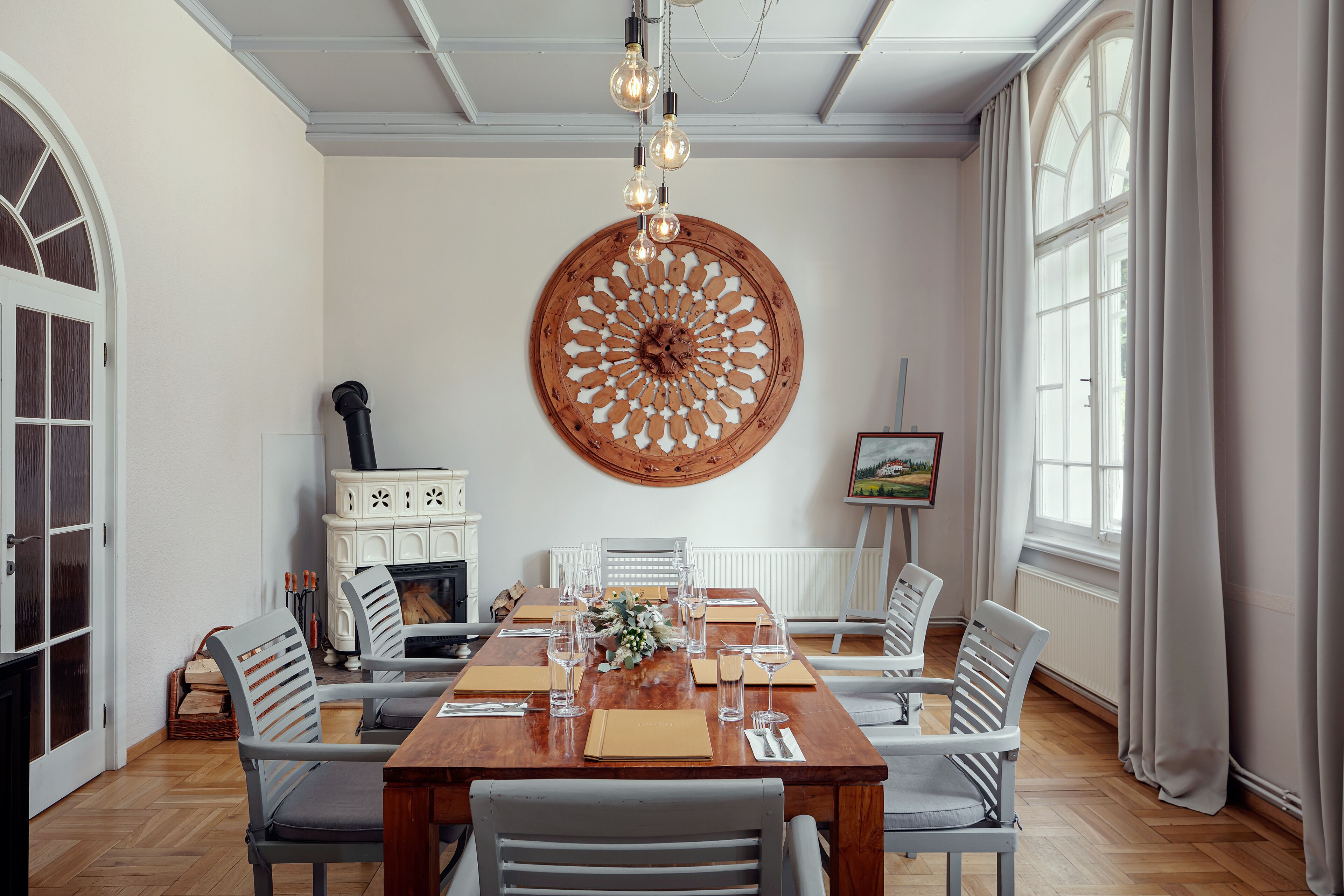 Comedor con una mesa de madera, sillas blancas y un gran adorno en la pared.