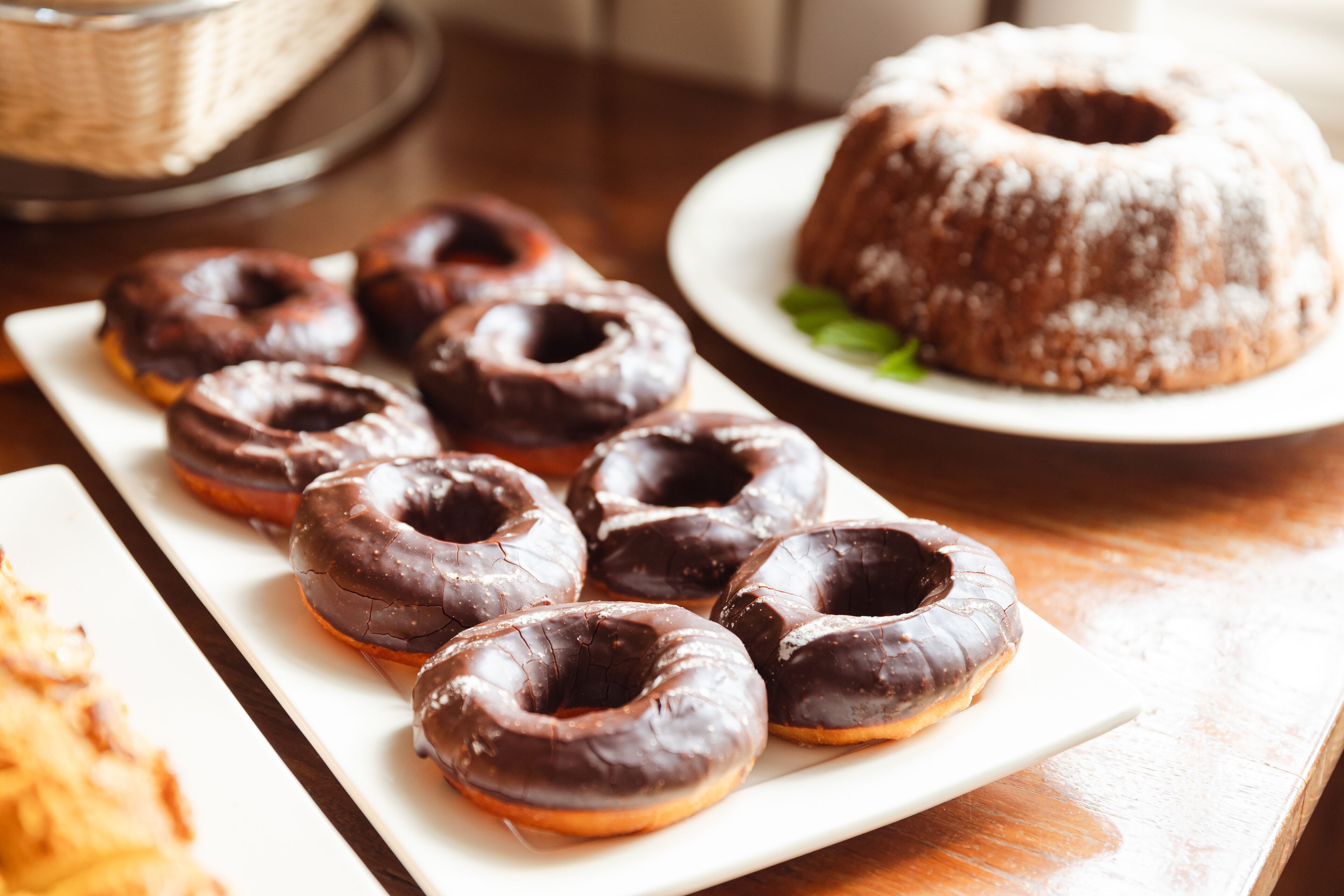 A plate of chocolate-glazed donuts and a bundt cake on a wooden table.
