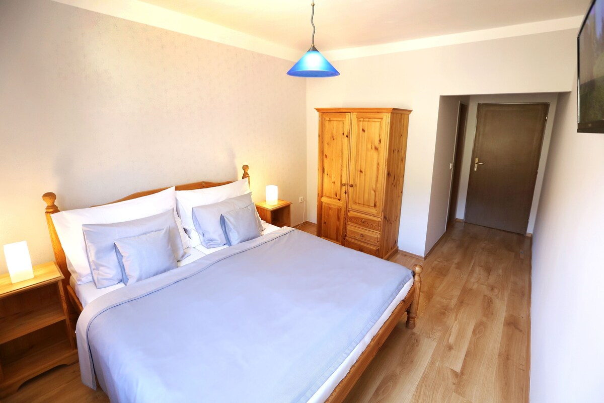 Un dormitorio con cama, armario de madera, mesitas de noche y una puerta.