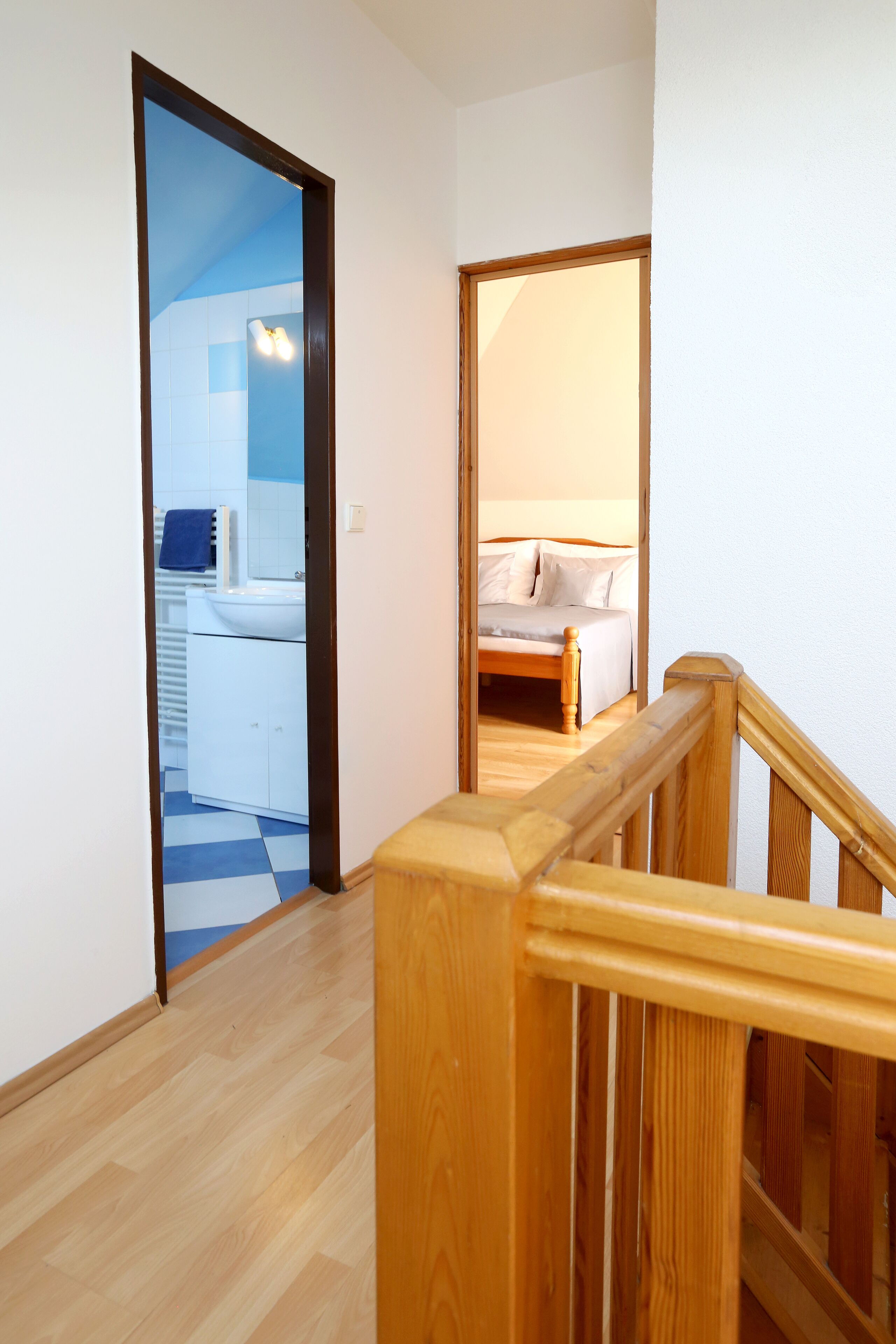 Ein Flur mit Holzbalkon, der zu einem Schlafzimmer mit Bett und einem Badezimmer mit Waschbecken und Spiegel führt.