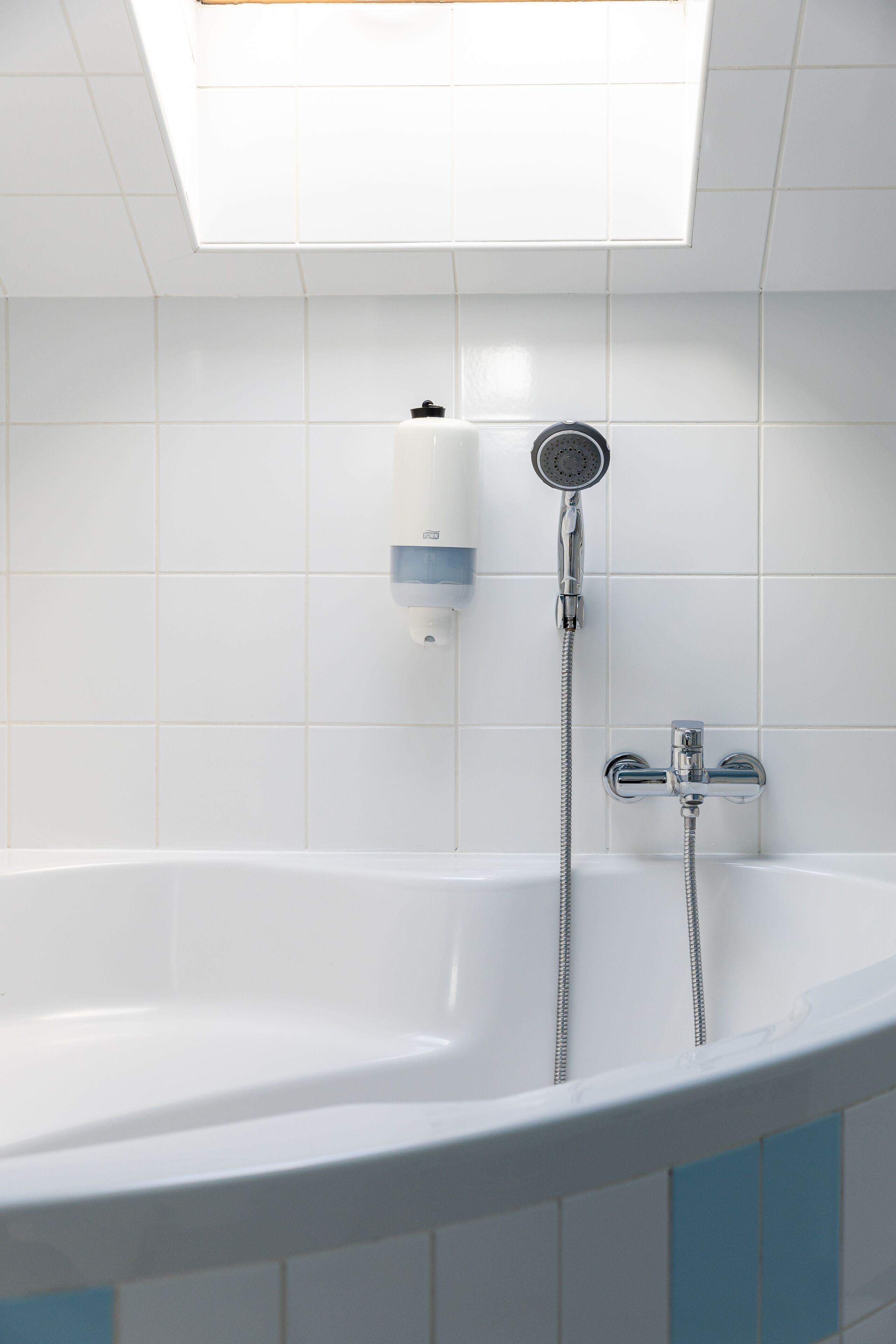 Un baño moderno con una bañera independiente, un cabezal de ducha de mano y un dispensador de jabón montado en la pared.