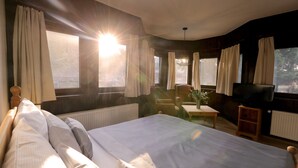 Una habitación de hotel con una cama grande, televisor, una mesita y cortinas en las ventanas.