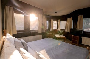 Una habitación de hotel con una cama grande, televisor, una mesita y cortinas en las ventanas.