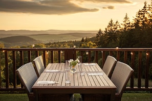 Una terraza de madera con una mesa dispuesta para comer, con vistas a un paisaje pintoresco de colinas y árboles.