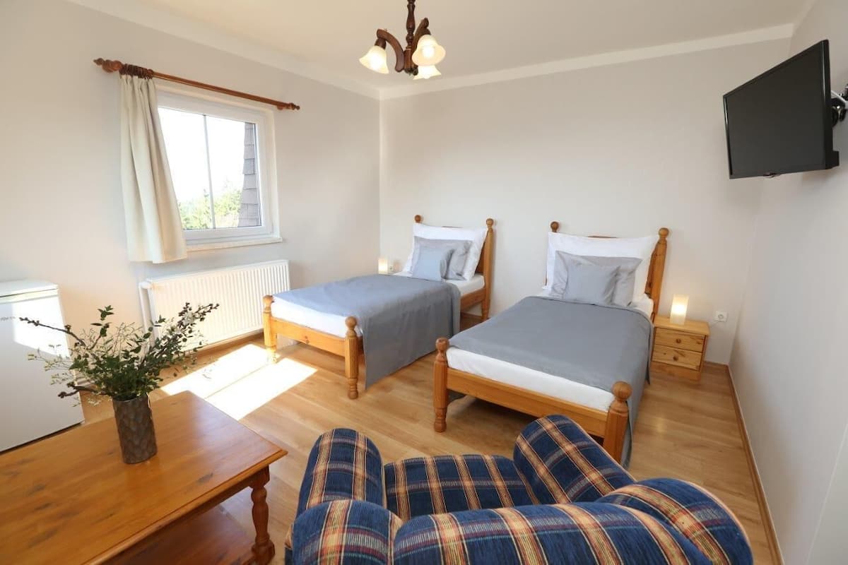 A room with two wooden beds, a wooden table, a chair, a TV, and a window with curtains.