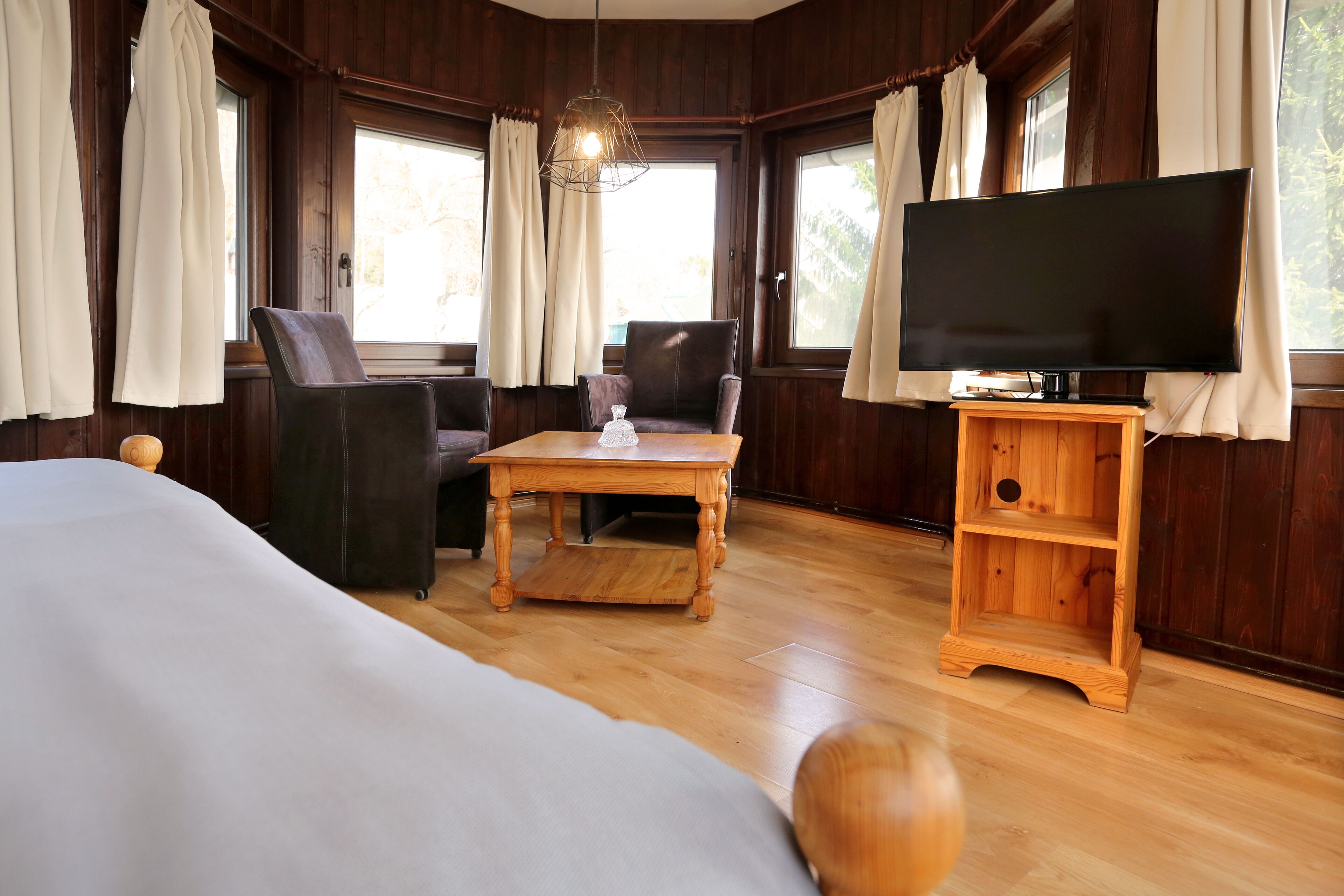 A room with a bed, a wooden table, a TV on a wooden stand, and two chairs.