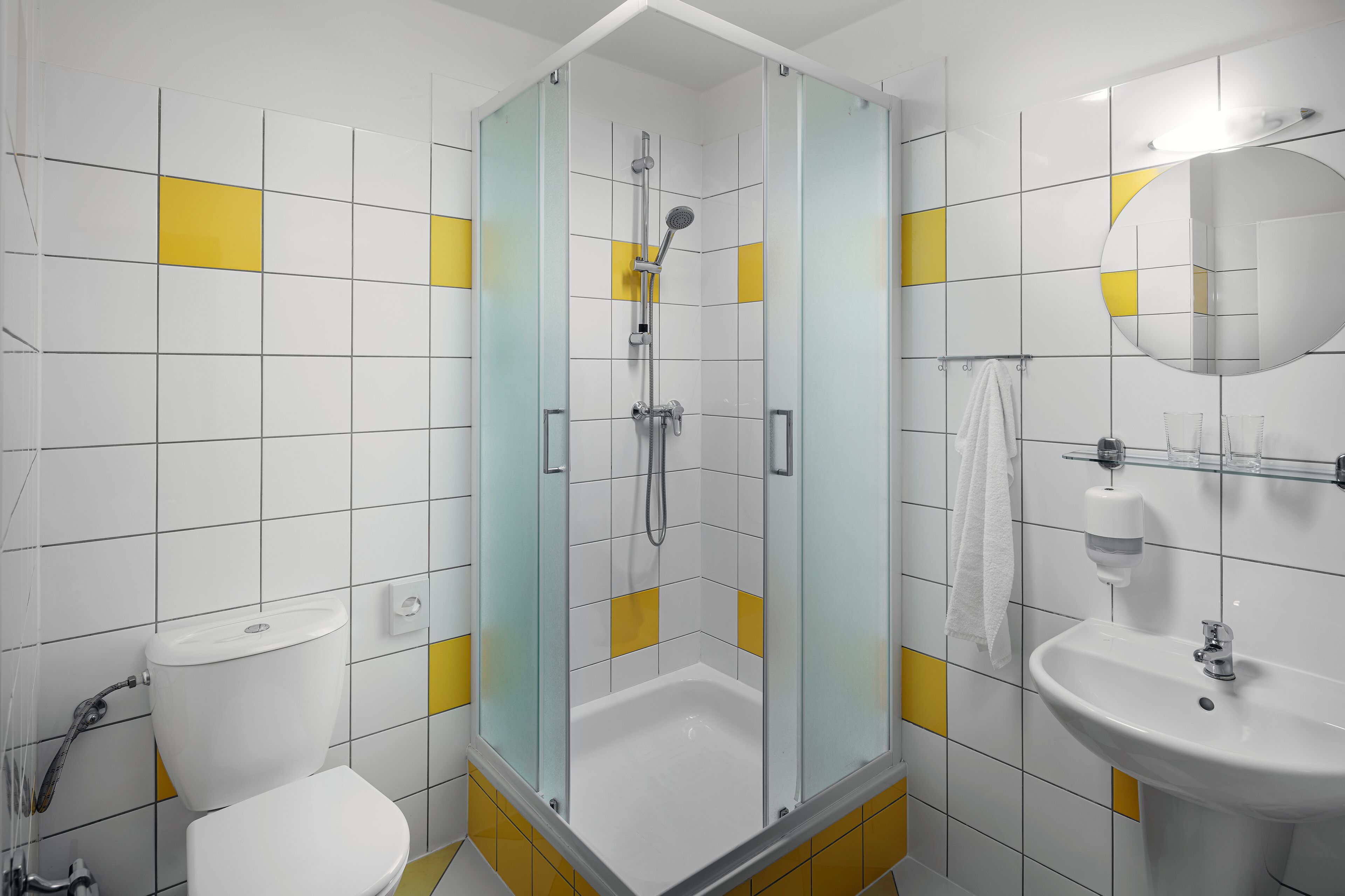 A modern bathroom with a glass-enclosed shower, a white sink, and yellow-tiled walls.