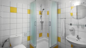 A modern bathroom with a glass-enclosed shower, a white sink, and yellow-tiled walls.