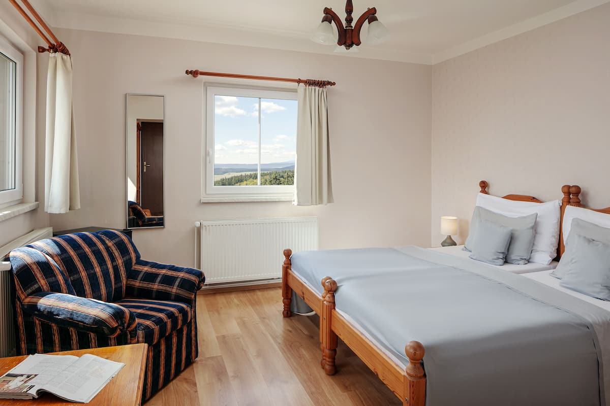 A bedroom with a bed, a chair, a window with curtains, a radiator, and a ceiling light fixture.