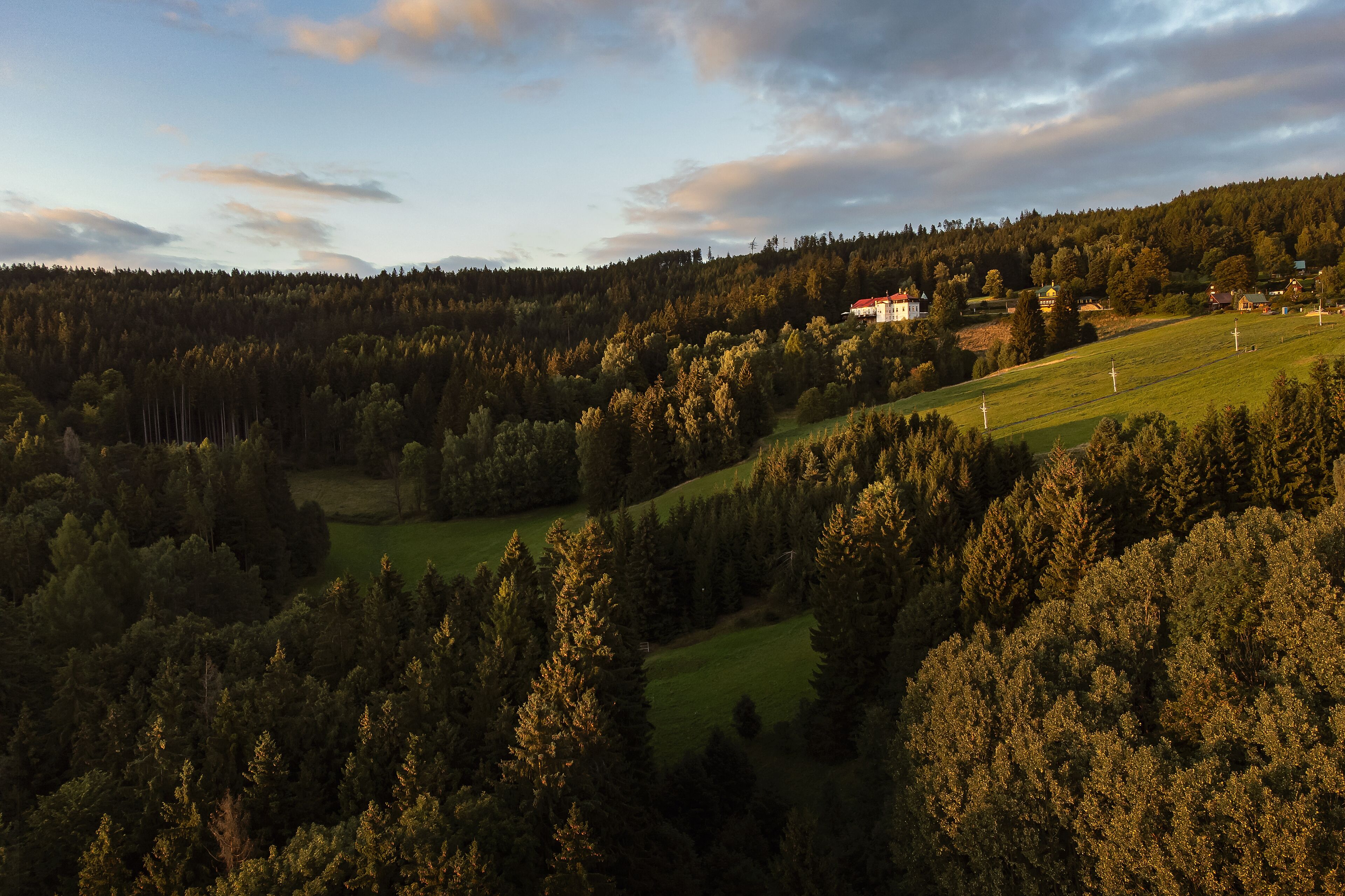 A rural landscape with a house on a hill, surrounded by dense forests and open fields.