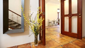 Un pasillo con puerta de madera, suelo de baldosas y un jarrón con flores amarillas en la pared.