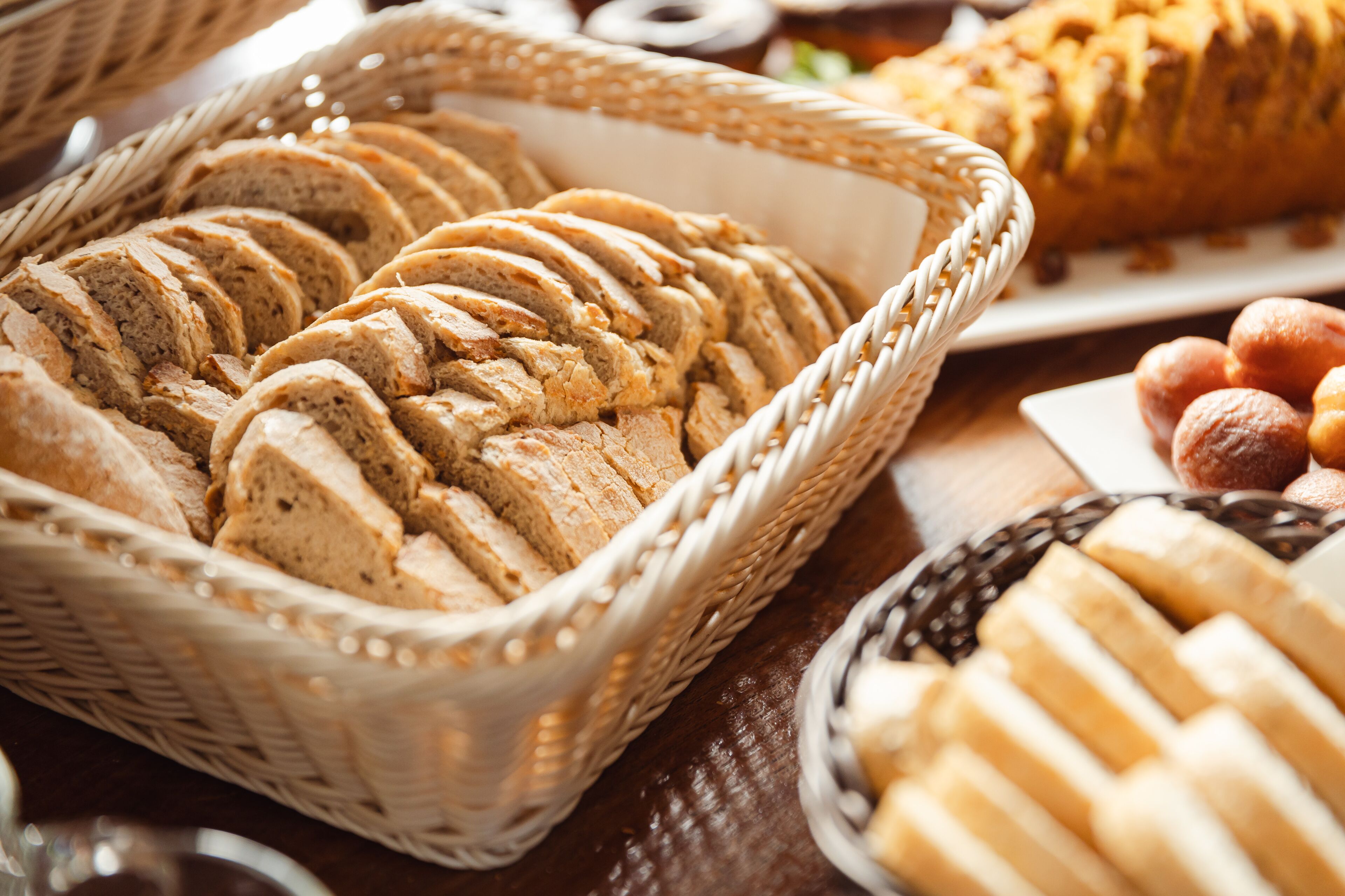 Une table où sont présentés différents types de pain et de viennoiseries, notamment des tranches de pain dans un panier et une miche de pain en arrière-plan.