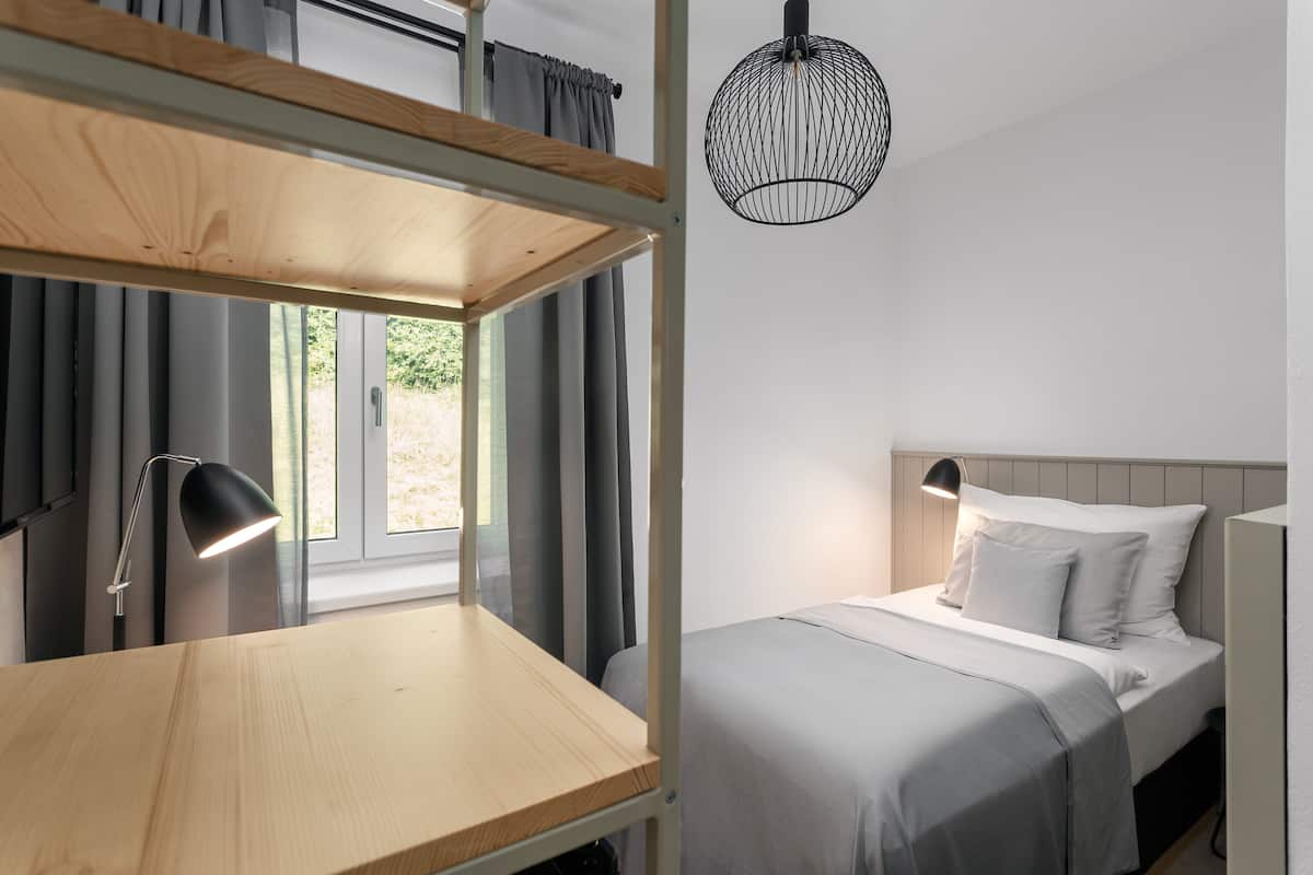 Een stapelbed met een bureau en lamp, een nachtkastje, een bed met kussens en een hangende lamp.