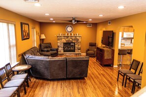 A living room with a sectional sofa, a fireplace, a clock, and a kitchen area with a microwave.