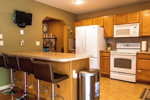A kitchen with wooden cabinets, a stainless steel refrigerator, a microwave, an oven, and a bar area with stools.