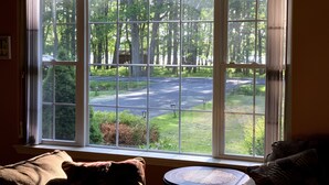 A room with a large window overlooking a road and greenery. There is a small round table with a placemat in front of the window. - Gorgeous Villa in Pocono nr Ski Slopes, Camelback, Kalahari w Games Rm & Hot tub (Pocono Summit)