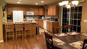 A modern kitchen with wooden cabinets, a refrigerator, a microwave, and a dining area with a table and chairs. - Gorgeous Villa in Pocono nr Ski Slopes, Camelback, Kalahari w Games Rm & Hot tub (Pocono Summit)