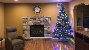 A living room with a stone fireplace, a Christmas tree, and a clock on the wall. - Gorgeous Villa in Pocono nr Ski Slopes, Camelback, Kalahari w Games Rm & Hot tub (Pocono Summit)