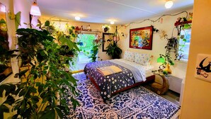 A bedroom with a bed, a patterned rug, and various plants.