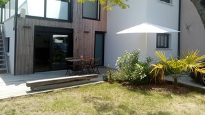 A modern house with a wooden exterior, a glass door entrance, a patio with a table and chairs, and a white umbrella.