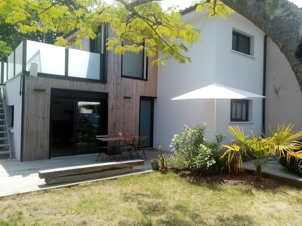 A modern house with a wooden exterior, a glass door entrance, a patio with a table and chairs, and a white umbrella.
