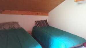 Una stanza piccola con due letti singoli, ciascuno con copriletto verde. La stanza presenta un soffitto in legno e pareti bianche.