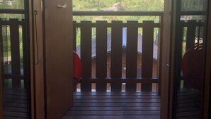 Una porta di legno aperta che dà su un balcone con vista su una valle verde e montagne.