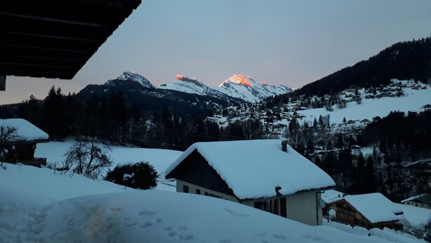 Paesaggio montano innevato con un piccolo villaggio e case ricoperte di neve.