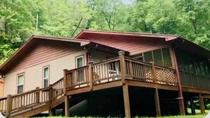 A two-story cabin with a wooden deck and a covered porch.