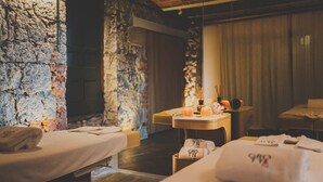 A spa room with two massage beds, a wooden table with candles and a clock, and a stone wall. - Tremonti Ski Bike Resort (Karpacz)