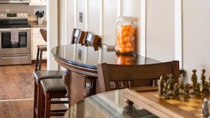 Un comedor con mesa de vidrio, sillas de madera, un tablero de ajedrez y un frasco de bocadillos.