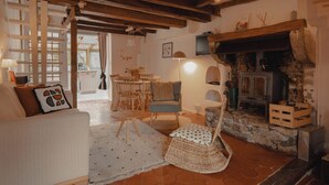 A cozy living room with a fireplace, wooden beams, a dining area, and a sofa.