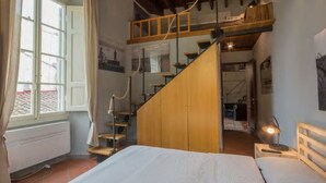 Ein Schlafzimmer mit einem Bett, einem Schlafzimmerboden aus Holz, einer Treppe und einem Fenster mit Vorhängen.