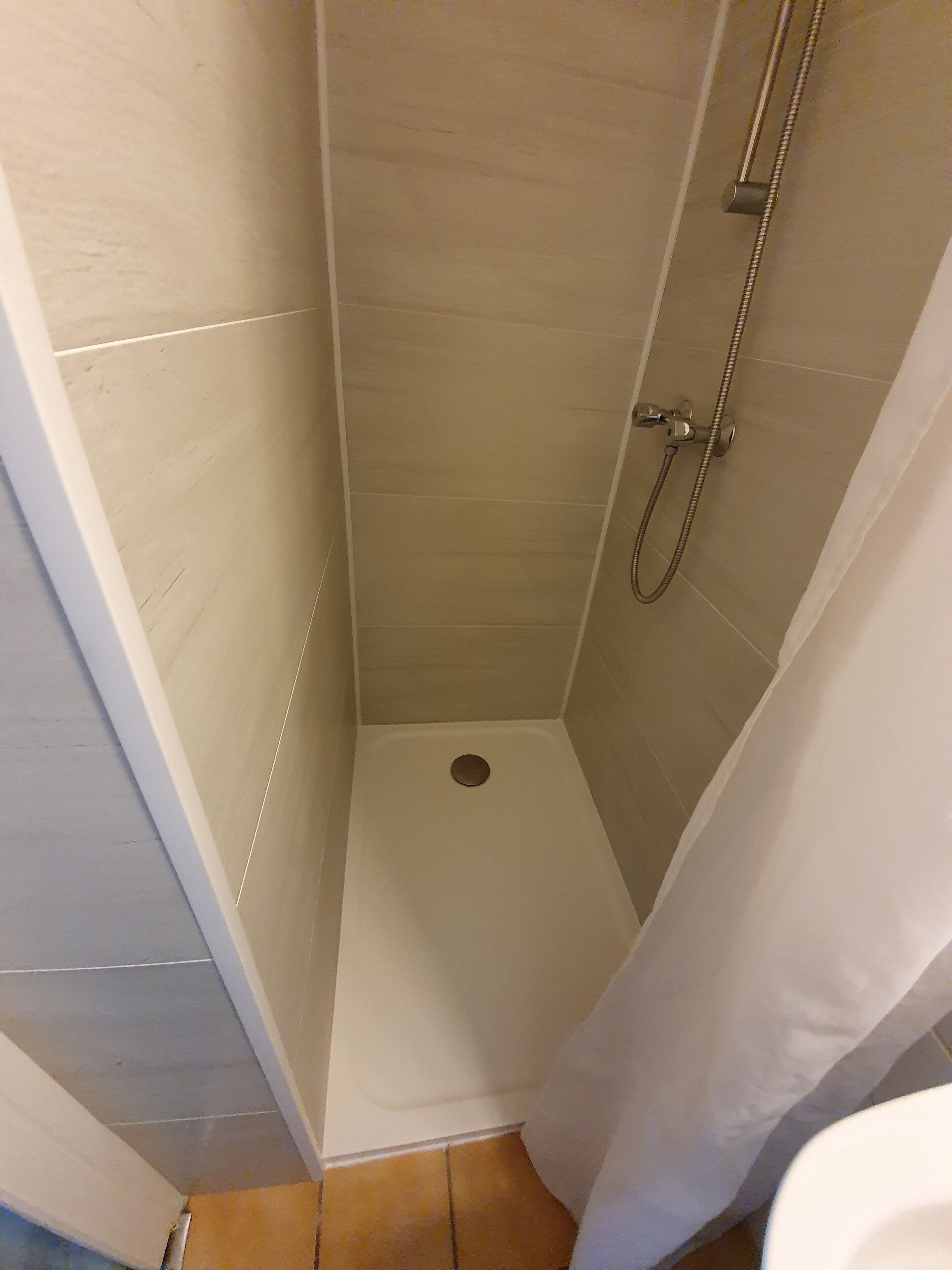 A small, enclosed shower area with a drain in the center, tiled walls, and a showerhead mounted on the wall.