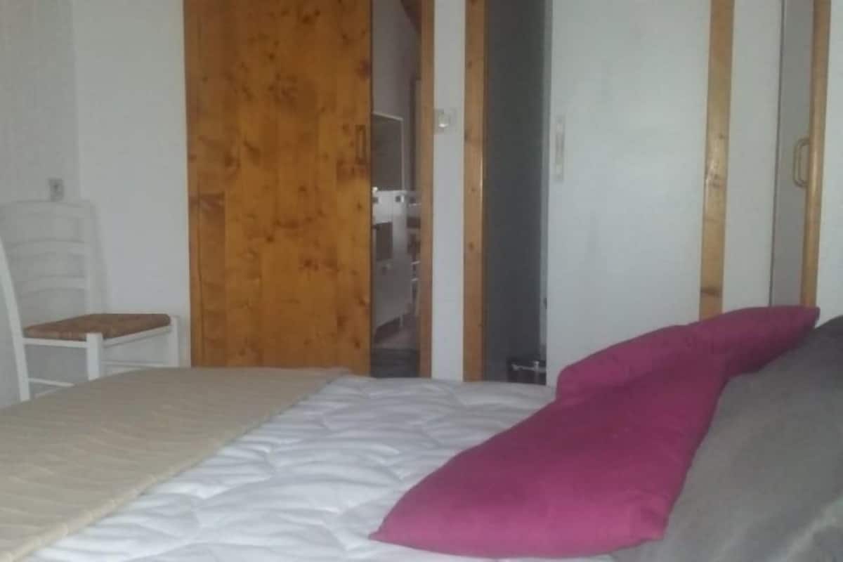 Ein Schlafzimmer mit einem Bett, einem Holzschrank und einem weißen Stuhl.