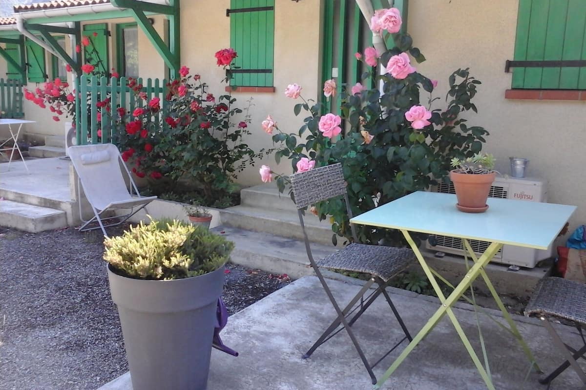 Eine Terrassenfläche mit Sitzgelegenheiten im Freien, einem Blumentopf und einem Gebäude mit grünen Fensterläden.